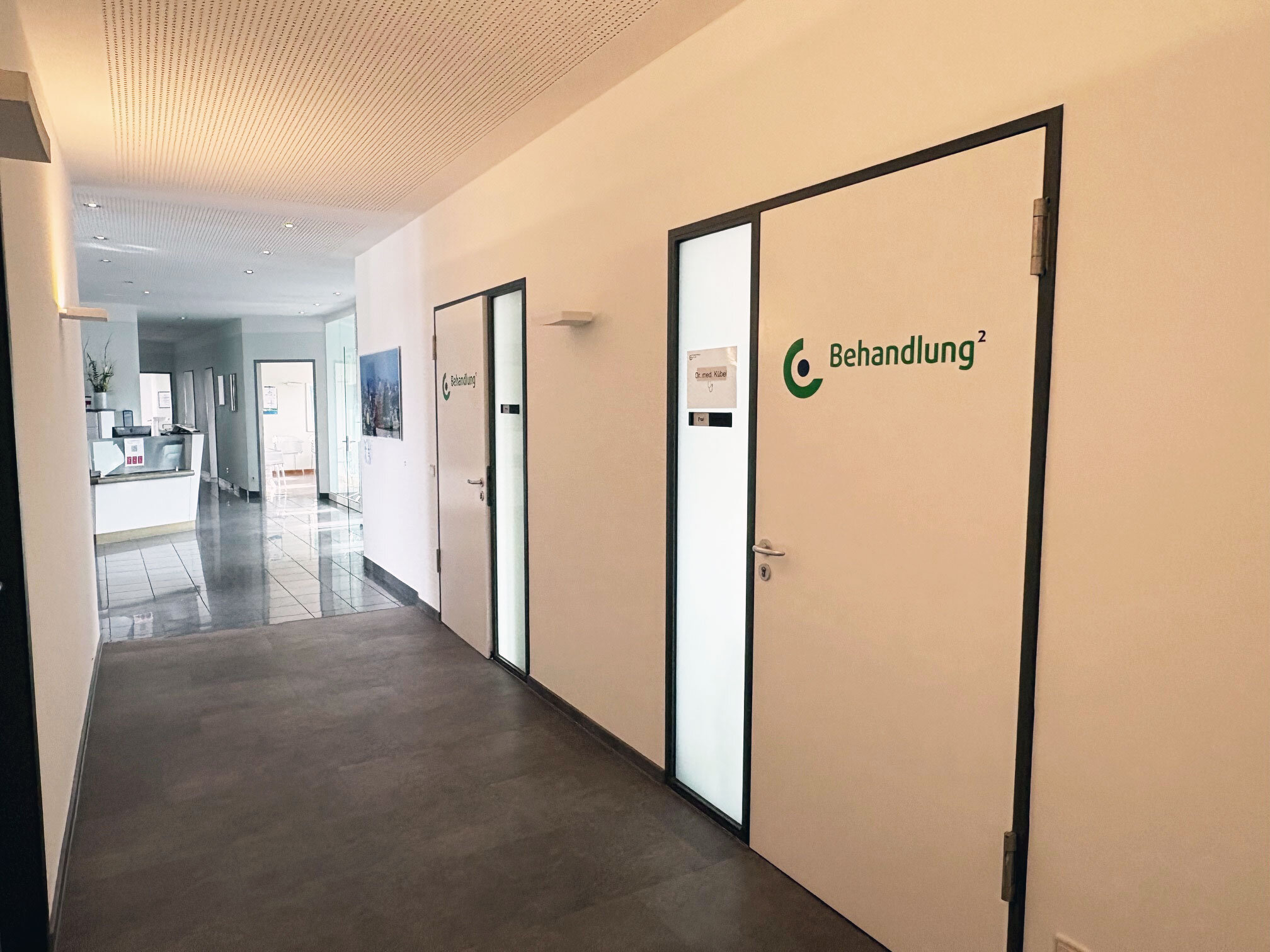 Heller Flur im Ärztezentrum Einsteinstraße mit Tür „Behandlung²“, Schild und Empfangsbereich.