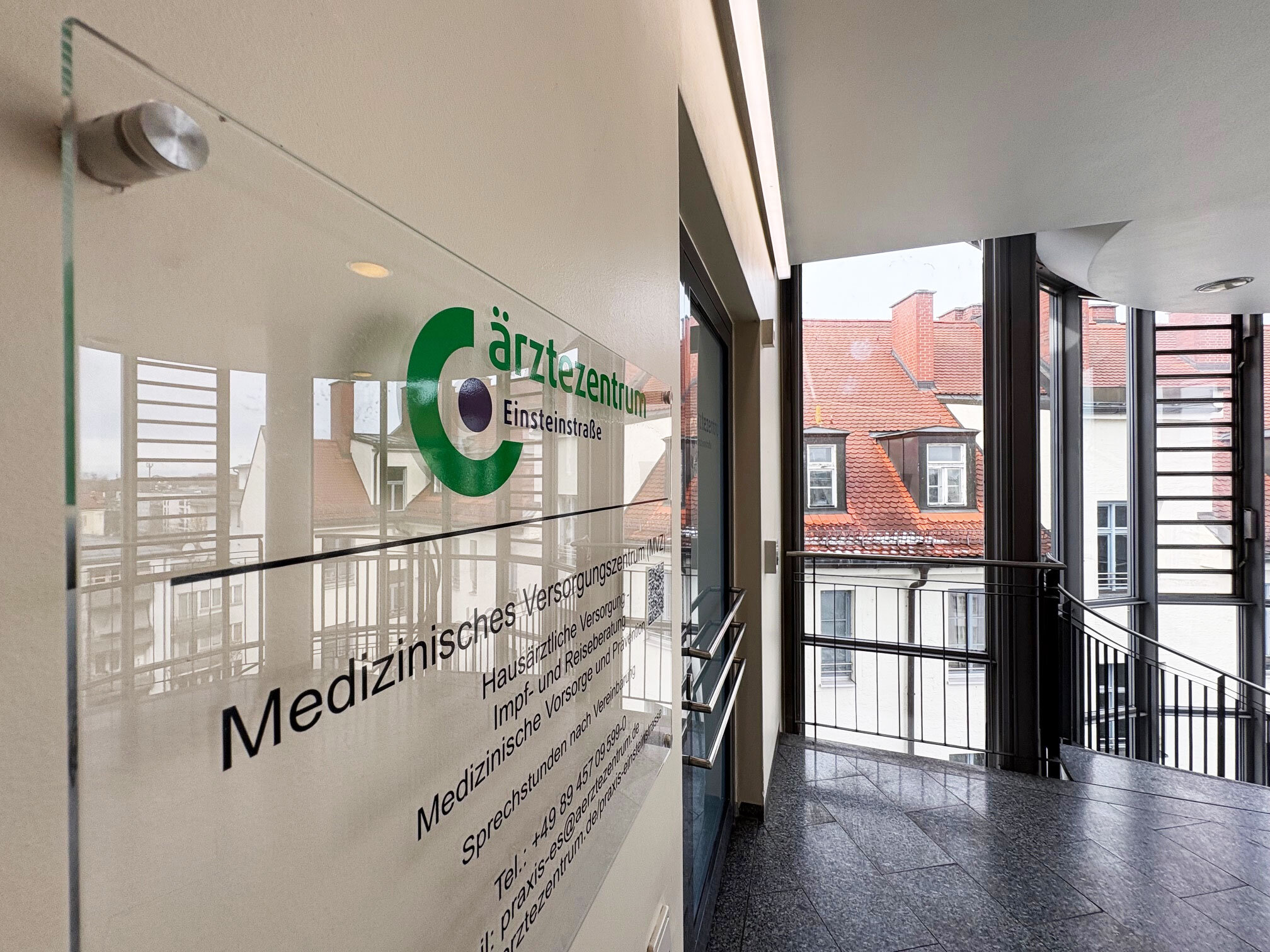 Helles Treppenhaus mit Glas-Schild „Ärztezentrum Einsteinstraße“ modern gestaltet.