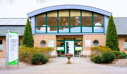 Eingangsbereich des Ärztezentrum Gorch Fock mit moderner Glasfront, rotem Backstein und gepflegtem Vorgarten.